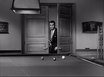 Movie still from “A Place in the Sun” (1951), directed by George Stevens – A black and white photo of a man standing in a doorway; Wide shot, High angle
