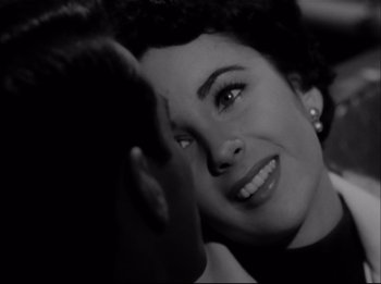 Movie still from “A Place in the Sun” (1951), directed by George Stevens – A woman smiles at the camera while a man looks at her face; Close Up shot, High angle