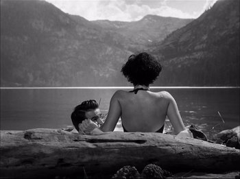 Movie still from “A Place in the Sun” (1951), directed by George Stevens – A man and a woman sitting on a log in the water; Wide shot, High angle