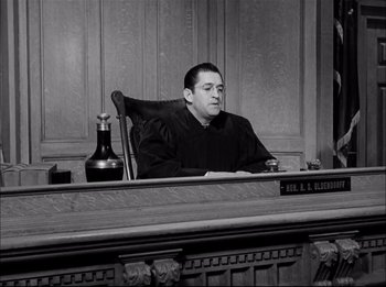 Movie still from “A Place in the Sun” (1951), directed by George Stevens – A man sitting at a judge's desk in a courtroom; Medium shot, Low angle