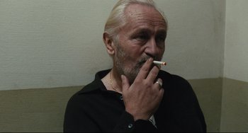 Movie still from “A Prophet” (2009), directed by Jacques Audiard – An older man smoking a cigarette while sitting down; Close Up shot, Low angle