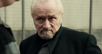 Movie still from “A Prophet” (2009), directed by Jacques Audiard – An old man with a beard and a black jacket; Close Up shot, Low angle