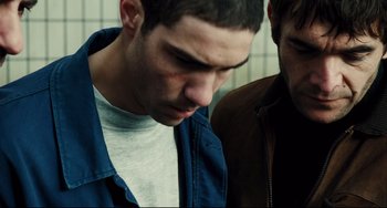 Movie still from “A Prophet” (2009), directed by Jacques Audiard – A man with a bruised face looking down at another man; Close Up shot, Over the shoulder angle