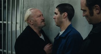 Movie still from “A Prophet” (2009), directed by Jacques Audiard – A man and a boy standing next to each other in front of a cement wall; Medium shot, Over the shoulder angle