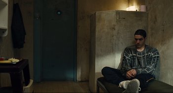 Movie still from “A Prophet” (2009), directed by Jacques Audiard – A man sitting on a chair in a room; Medium shot, Over the shoulder angle