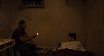 Movie still from “A Prophet” (2009), directed by Jacques Audiard – Two men sitting on a bed in a dark room; Medium shot, High angle