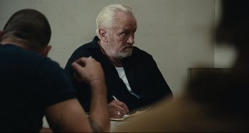 Movie still from “A Prophet” (2009), directed by Jacques Audiard – An older man sitting at a table with a pen in his hand; Close Up shot, Over the shoulder angle