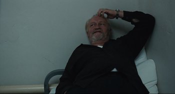 Movie still from “A Prophet” (2009), directed by Jacques Audiard – An older man sitting on a chair with his hand on his head; Close Up shot, Low angle