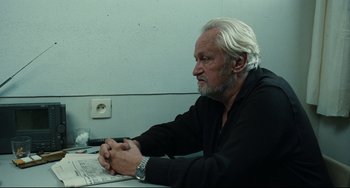 Movie still from “A Prophet” (2009), directed by Jacques Audiard – An older man sitting in front of a computer keyboard; Medium shot, Over the shoulder angle