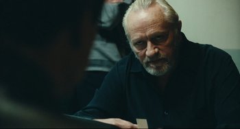 Movie still from “A Prophet” (2009), directed by Jacques Audiard – An older man sitting at a table looking at a computer screen; Close Up shot, Over the shoulder angle