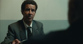 Movie still from “A Prophet” (2009), directed by Jacques Audiard – An older man wearing a suit and tie; Close Up shot, Over the shoulder angle