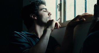 Movie still from “A Prophet” (2009), directed by Jacques Audiard – A man sitting in front of a window holding a cigarette in his mouth; Close Up shot, Low angle