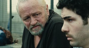 Movie still from “A Prophet” (2009), directed by Jacques Audiard – An older man and a younger man looking at one another; Close Up shot, Over the shoulder angle