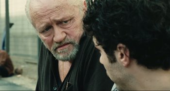 Movie still from “A Prophet” (2009), directed by Jacques Audiard – An older man and a younger man are talking together; Close Up shot, Over the shoulder angle