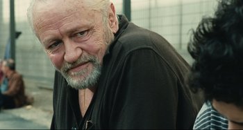 Movie still from “A Prophet” (2009), directed by Jacques Audiard – An older man with a beard and a mustache; Close Up shot, Over the shoulder angle