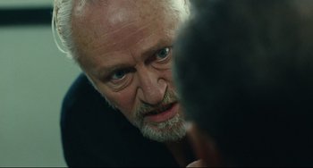 Movie still from “A Prophet” (2009), directed by Jacques Audiard – An older man with a goatee looking at the camera; Close Up shot, Over the shoulder angle