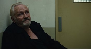 Movie still from “A Prophet” (2009), directed by Jacques Audiard – An older man sitting in a chair in front of a wall; Close Up shot, Over the shoulder angle