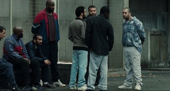 Movie still from “A Prophet” (2009), directed by Jacques Audiard – A group of men standing next to each other on a sidewalk; Wide shot, Over the shoulder angle