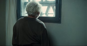 Movie still from “A Prophet” (2009), directed by Jacques Audiard – An older person looking out of a window; Medium shot, Over the shoulder angle