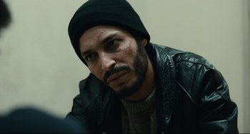 Movie still from “A Prophet” (2009), directed by Jacques Audiard – A person wearing a hat and a leather jacket; Close Up shot, Over the shoulder angle
