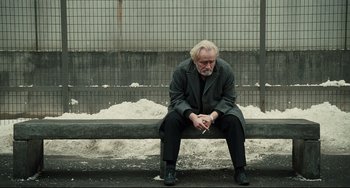 Movie still from “A Prophet” (2009), directed by Jacques Audiard – An older man sitting on a bench with a cigarette in his mouth; Wide shot, Over the shoulder angle
