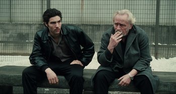 Movie still from “A Prophet” (2009), directed by Jacques Audiard – Two men sitting on a bench one smoking a cigarette; Medium shot, Low angle
