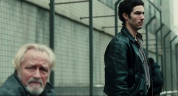 Movie still from “A Prophet” (2009), directed by Jacques Audiard – A man standing next to another man wearing a leather jacket; Medium shot, Over the shoulder angle