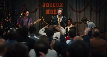 Movie still from “A Prophet” (2009), directed by Jacques Audiard – A group of people sitting on a stage with a man playing a saxophone; Medium shot, Over the shoulder angle