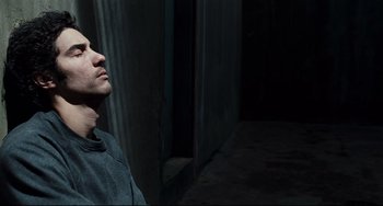 Movie still from “A Prophet” (2009), directed by Jacques Audiard – A man standing next to a wall in a dark room; Close Up shot, Overhead angle