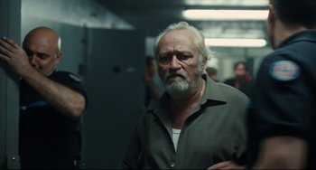 Movie still from “A Prophet” (2009), directed by Jacques Audiard – An old man with a beard is standing in a room; Medium shot, Over the shoulder angle