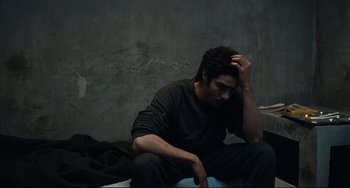 Movie still from “A Prophet” (2009), directed by Jacques Audiard – A man sitting on the ground with his head in his hand; Medium shot, Overhead angle