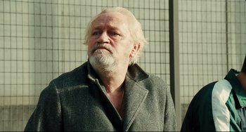 Movie still from “A Prophet” (2009), directed by Jacques Audiard – An older man with a beard and a gray coat; Close Up shot, Low angle