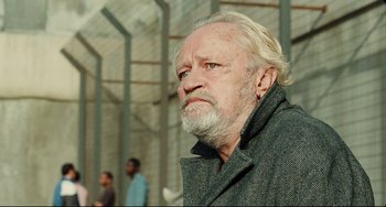 Movie still from “A Prophet” (2009), directed by Jacques Audiard – An older man with a beard and a gray jacket; Close Up shot, Over the shoulder angle