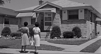 Two women are walking down the sidewalk in front of a house