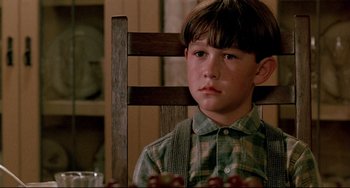 Movie still from “A River Runs Through It” (1992), directed by Robert Redford – A young boy sitting in a chair in a room; Close Up shot, Low angle