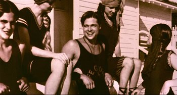 Movie still from “A River Runs Through It” (1992), directed by Robert Redford – A man sitting on the ground next to two other women; Medium shot, Low angle