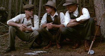 Movie still from “A River Runs Through It” (1992), directed by Robert Redford – A group of men sitting next to each other in the woods; Medium shot, Low angle