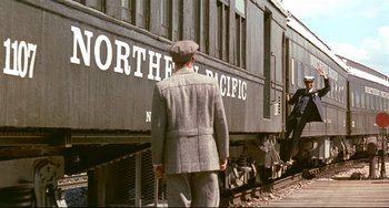 Movie still from “A River Runs Through It” (1992), directed by Robert Redford – A man standing on the side of a train car; Wide shot, Over the shoulder angle