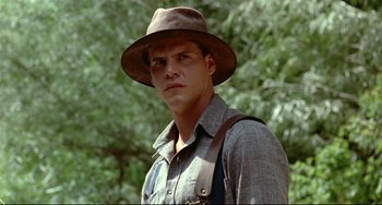 Movie still from “A River Runs Through It” (1992), directed by Robert Redford – A man wearing a hat and suspenders in front of trees; Close Up shot, Low angle