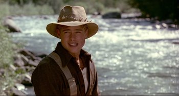 Movie still from “A River Runs Through It” (1992), directed by Robert Redford – A man in a hat standing in front of a river; Close Up shot, Over the shoulder angle