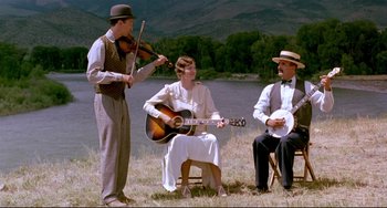 Movie still from “A River Runs Through It” (1992), directed by Robert Redford – A group of people sitting in the grass playing music; Wide shot, Low angle