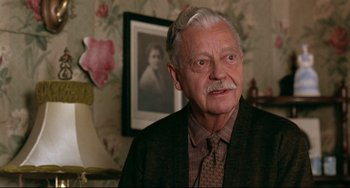Movie still from “A River Runs Through It” (1992), directed by Robert Redford – An older man wearing a suit and tie in front of a picture; Close Up shot, Low angle