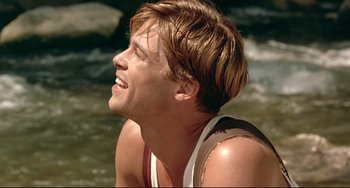Movie still from “A River Runs Through It” (1992), directed by Robert Redford – A young man in a tank top sitting in the water; Close Up shot, Over the shoulder angle
