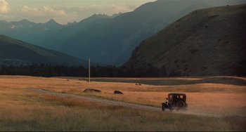 Movie still from “A River Runs Through It” (1992), directed by Robert Redford – An old car driving down a dirt road in the middle of a field; Extreme Wide shot, Low angle