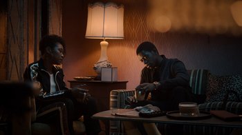 Movie still from “Snowfall” (2017), directed by Hiro Murai – A man and a woman sitting at a table playing cards; Medium shot, Low angle