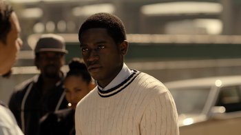Movie still from “Snowfall” (2017), directed by Hiro Murai – A young man in a white sweater is looking at the camera; Close Up shot, Over the shoulder angle