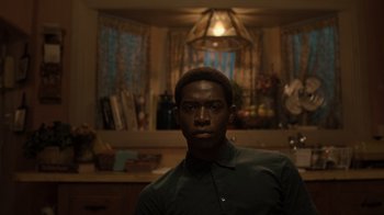 Movie still from “Snowfall” (2017), directed by Hiro Murai – A man standing in a room with a light on the wall behind him; Medium shot, Over the shoulder angle