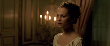 Movie still from “A Royal Affair” (2012), directed by Nikolaj Arcel – A woman in a white dress standing in front of candles; Close Up shot, Over the shoulder angle