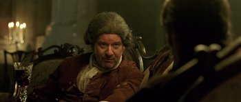 Movie still from “A Royal Affair” (2012), directed by Nikolaj Arcel – A man in a wig sitting in a chair; Close Up shot, Over the shoulder angle