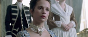 Movie still from “A Royal Affair” (2012), directed by Nikolaj Arcel – A young woman wearing a dress and a necklace; Close Up shot, Over the shoulder angle